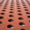 Rows of textured, reddish-brown Food Production Mats with circular holes arranged in a grid pattern create a geometric and symmetrical design, revealing blue surfaces through the openings.