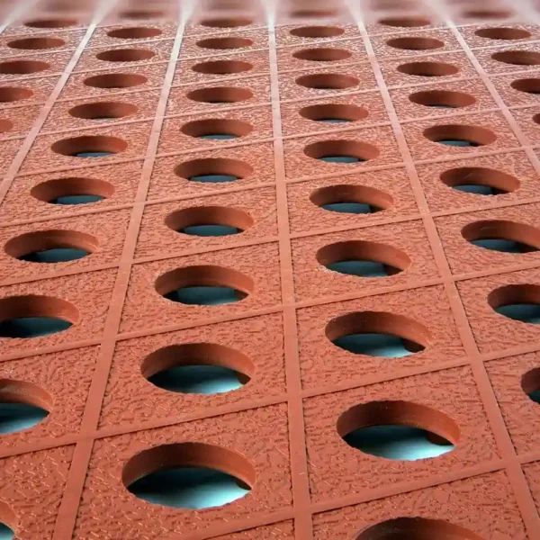 Rows of textured, reddish-brown Food Production Mats with circular holes arranged in a grid pattern create a geometric and symmetrical design, revealing blue surfaces through the openings.