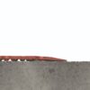 The Food Production Mat, a red textured tile with raised circular bumps, rests unevenly on a rough concrete slab against a plain white background.
