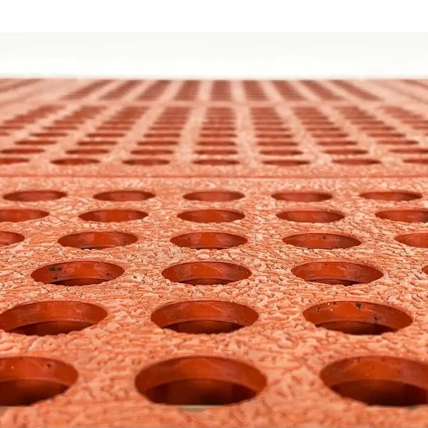 Close-up of the Interlocking Catering Mat, featuring an orange rubber design with a textured surface and evenly spaced round holes, photographed from a low angle.