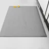 An Anti-Static Mat in grey is placed on a white floor next to a white wall with a black skirting board. A yellow measuring tape is coiled and resting near the top left corner of the mat.