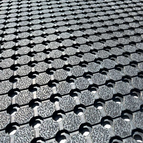 Close-up of the Anti-Slip Mat, showing its textured rubber surface with a repeating hexagonal and circular hole pattern for enhanced grip and drainage, photographed at an angle.