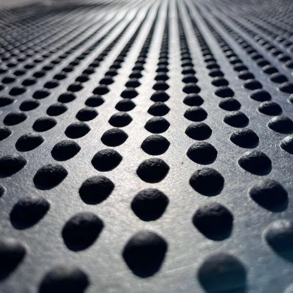 Close-up of the Raised Top Stable Mat’s metal surface, featuring evenly spaced raised circular bumps in rows. Reflected light emphasises the textured, repeating pattern and sense of depth.