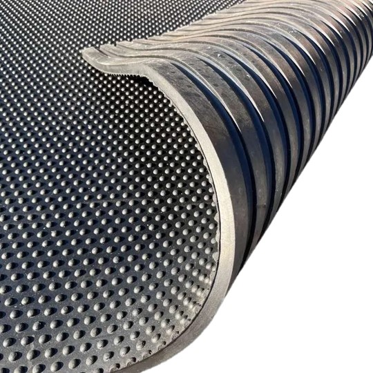 A close-up of the Raised Top Stable Mat, a black rubber mat featuring a raised dot pattern on one side and grooves on the other, partially rolled to display both textured surfaces.