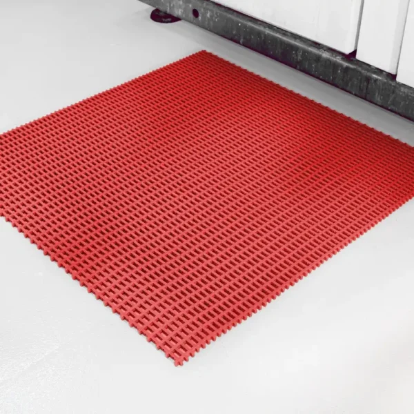 A Heavy-Duty Cross-Ribbed Mat in red rubber with a square grid pattern is placed on a light grey floor near a cupboard.