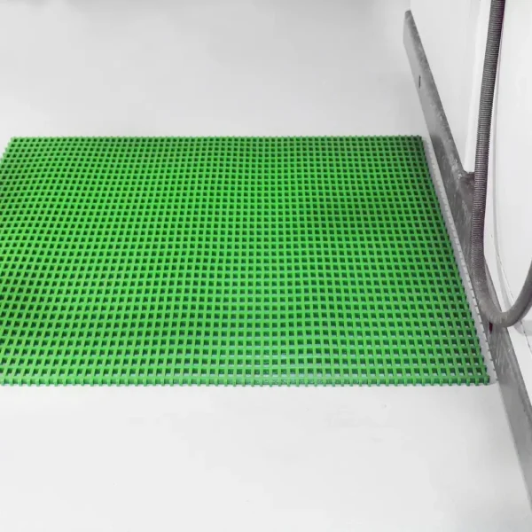 The Heavy-Duty Cross-Ribbed Mat, bright green and rubber with a grid pattern, is placed on a clean white floor near a wall with a metal skirting board and an attached grey hose.
