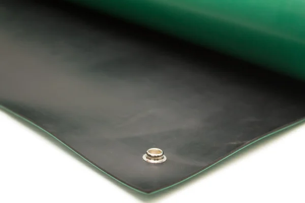 Close-up of Conductive Rubber Bench Matting in black, featuring a metal eyelet on one edge, displayed on a white surface and partially covered by a green layer.