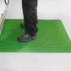 A person in black trousers and shoes stands on a bright green Premium Cross-Ribbed Mat, which is laid over a light grey floor.