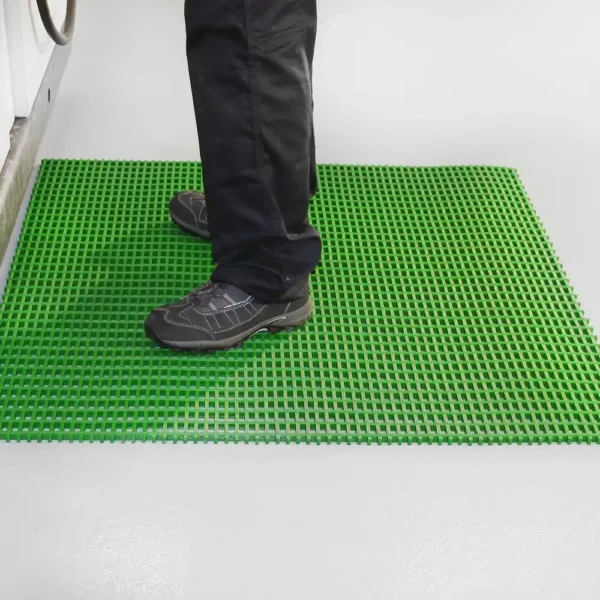 A person in black trousers and shoes stands on a bright green Premium Cross-Ribbed Mat, which is laid over a light grey floor.