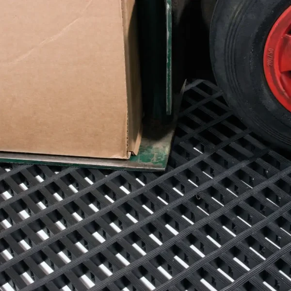 A cardboard box sits on a metal trolley with a red wheel, positioned on the black Premium Cross-Ribbed Mat.