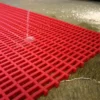 Water flows onto a Premium Cross-Ribbed Mat on a concrete floor, easily passing through its red plastic grid openings.