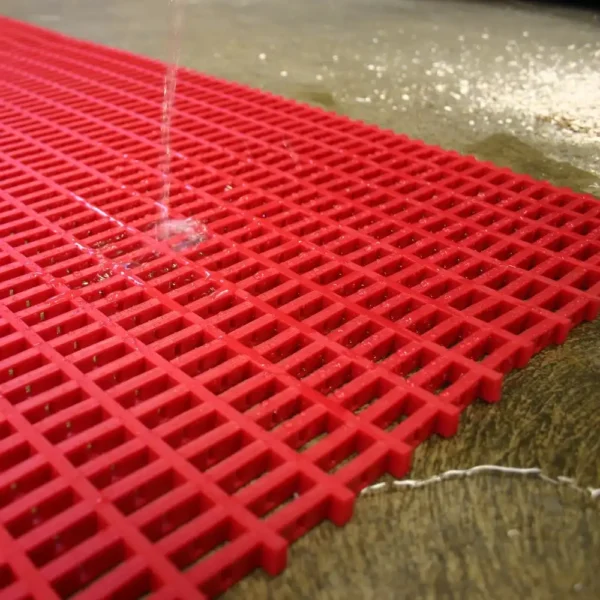 Water flows onto a Premium Cross-Ribbed Mat on a concrete floor, easily passing through its red plastic grid openings.