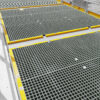 Open Top Grating with yellow safety edges is installed on an elevated platform, providing drainage and ventilation through its grid pattern; handrails in the background offer extra safety.