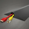 A PVC Cable Protector (HD) in black rests on a grey surface, neatly organising a red HDMI cable and a yellow Ethernet cable as they emerge from one end.