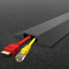 A PVC Cable Protector (Data) in black with two internal channels holds a red HDMI cable and a yellow Ethernet cable, resting on a dark carpeted surface.