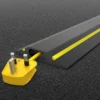 A yellow electrical plug and cable are partially covered by a PVC Cable Protector (GP) in black and yellow on a dark carpeted surface.