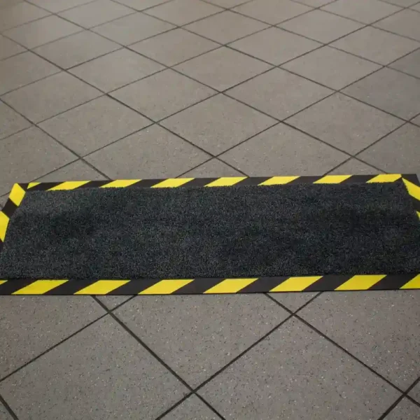 The Cable Protector Mat is a rectangular black floor mat with yellow and black caution stripes around the edges, placed on a tiled floor.