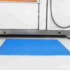 A Standard Cross-Ribbed Mat in blue with a grid pattern is placed on the floor in front of a washing machine and cupboards.