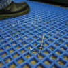 A close-up of a black shoe standing on the Standard Cross-Ribbed Mat, with blue anti-fatigue material trapping metal shavings and debris in its grid pattern.