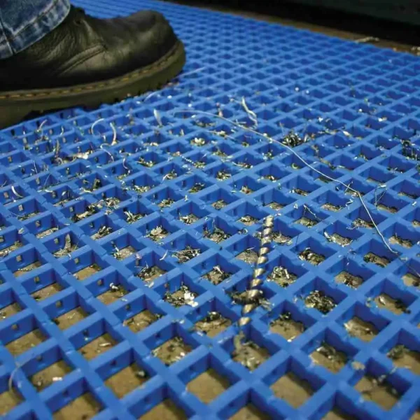 A close-up of a black shoe standing on the Standard Cross-Ribbed Mat, with blue anti-fatigue material trapping metal shavings and debris in its grid pattern.
