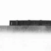 A Standard Cross-Ribbed Mat with a black plastic edging strip featuring rectangular slots is shown attached to the top of a textured grey concrete slab, viewed from the side against a white background.