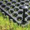 Close-up of an Interlocking Anti-Fatigue Mat, featuring circular holes, placed on grass with a large plastic peg securing it through one of the holes.