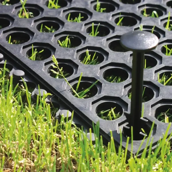 Close-up of an Interlocking Anti-Fatigue Mat, featuring circular holes, placed on grass with a large plastic peg securing it through one of the holes.
