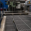 A factory workshop features metal machinery, wooden pallets, and Interlocking Anti-Fatigue Mats with circular holes on concrete floors, creating an organised industrial space with equipment in the background.