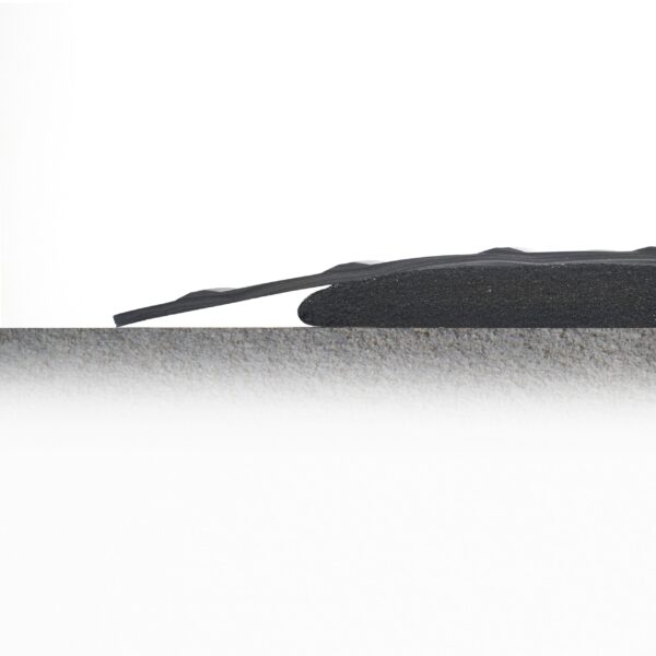 A Premium Anti-Fatigue Mat, thin, black, and flexible, rests slightly curved and elevated at one end on a textured grey surface against a white background.