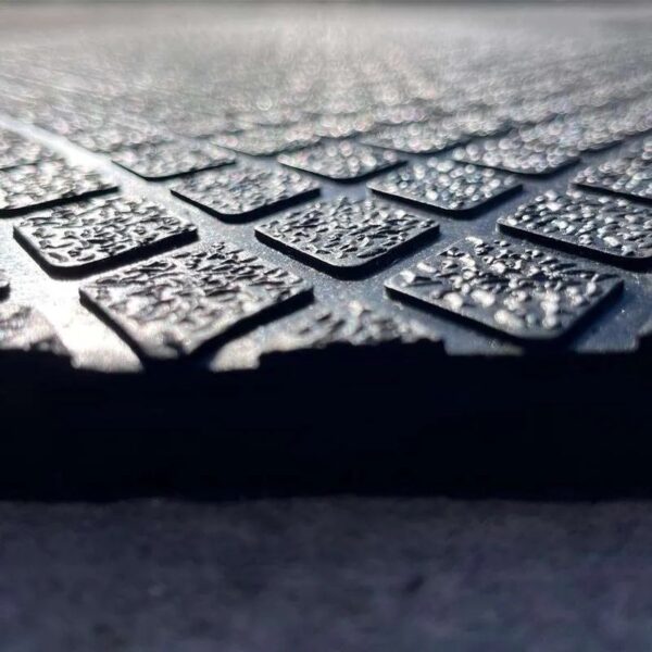 Close-up image of the Diamond Top Stable Mat’s textured, dark surface featuring a grid pattern with raised, bumpy squares, photographed at an angle to highlight its glistening, light-reflective finish.