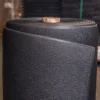A close-up of the ESD Textured Anti-Fatigue Mat, a large black rubber sheet with a cardboard core, rolled up and standing upright in an industrial environment.
