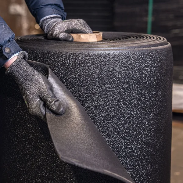 A person wearing gloves peels back a corner of a large rolled sheet of ESD Textured Anti-Fatigue Mat.