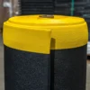A close-up of the ESD Textured Anti-Fatigue Mat, with a yellow top and black bottom, standing upright in a warehouse.