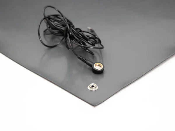 A black lead with a circular connector lies on an ESD Anti-Static Double Layer Sheet in dark grey featuring a metal press stud, set against a white background.