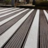 Close-up of dark wooden decking fitted with Anti-Slip Decking Strips in textured white, running parallel across the outdoor surface. The background features a blurred garden scene.