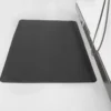 A Fine Ribbed Anti-Fatigue Mat in black is set on a light floor beside a metal workbench with a coiled cable hanging from the side.