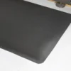 A close-up view of the Fine Ribbed Anti-Fatigue Mat in black, featuring slightly rounded corners on a white floor, with part of a metallic object visible at the top right edge.