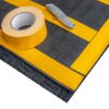 A forklift mat, featuring black material with yellow tape strips, is displayed alongside a roll of yellow adhesive tape and a utility knife on a white background.