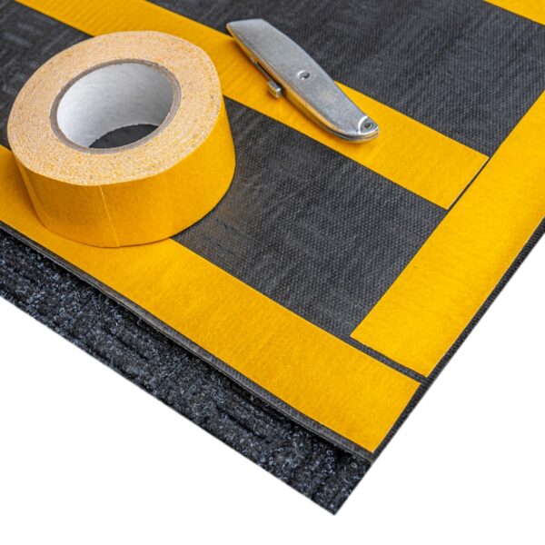 A forklift mat, featuring black material with yellow tape strips, is displayed alongside a roll of yellow adhesive tape and a utility knife on a white background.