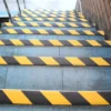 Concrete steps with each tread marked by GRP Grit Tape in black and yellow stripes, installed beside a brick wall with a metal handrail on the left.