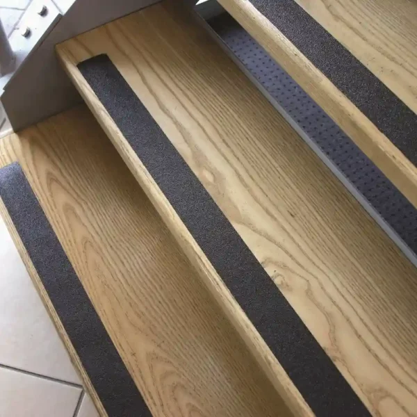 Wooden stairs with GRP Grit Tape black non-slip strips affixed to each step for added safety. The photo shows the steps from above at an angle, highlighting the textured GRP Grit Tape and wood grain.