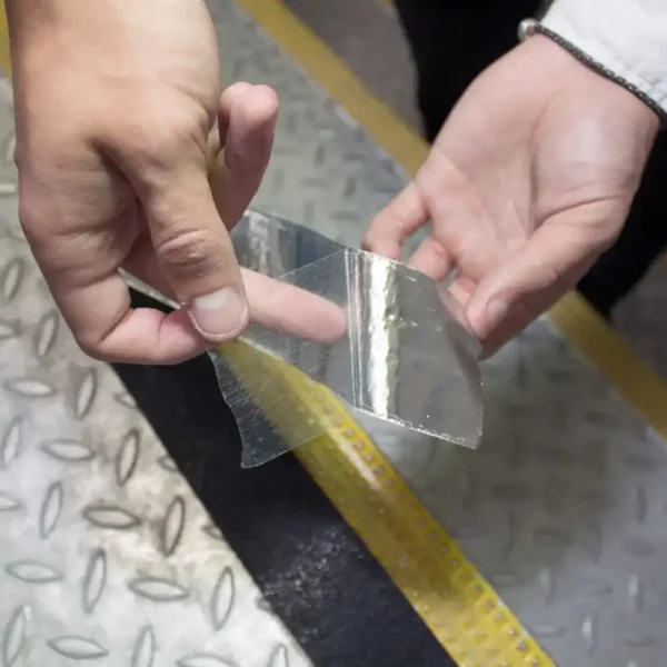 A person peels a strip of Anti-Slip Comfortable Tape from a chequered metal surface, next to a black strip and a yellow raised marker.