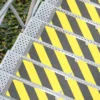 Aluminium Anti-Slip Stair Tread with yellow and black stripes installed on metal stairs, shown from above beside green ivy plants and a metal handrail.