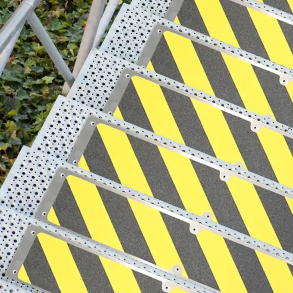 Aluminium Anti-Slip Stair Tread with yellow and black stripes installed on metal stairs, shown from above beside green ivy plants and a metal handrail.