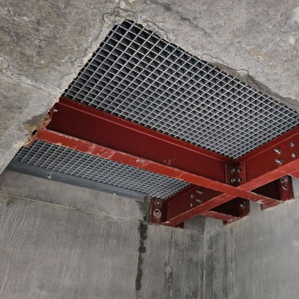 A ceiling view of a construction site shows red steel Angle Profiles supporting a metal grid panel, surrounded by unfinished concrete surfaces.