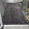 An Anti-Slip Flat Sheet with a dark, textured finish forms a wheelchair ramp bordered by metal railings on both sides, providing secure access to a higher level.