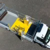 A white utility lorry with an open flatbed featuring bright yellow safety barriers and anti-slip flat sheet platforms is parked on a tarmac surface, viewed from above.