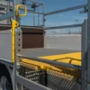 Close-up of a lorry featuring safety rails, a yellow handrail, and an Anti-Slip Flat Sheet platform. The lorry is parked near a barbed-wire metal fence under a blue sky.