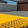 A close-up of the Anti-Slip Flat Sheet shows its textured grey surface, bright yellow edge, and grated yellow section, with metal railings and a building visible in the background.