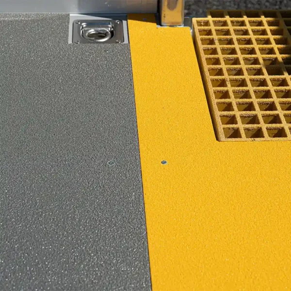 Close-up of a floor featuring the Anti-Slip Flat Sheet: textured grey surface on the left, smooth yellow centre, and a yellow grid-patterned mat on the right. A metal fixture is embedded in the top left corner.